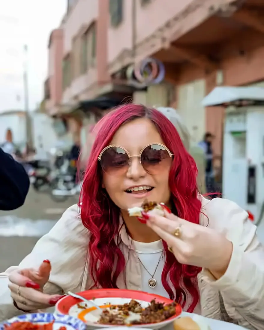 Smiling guest enjoying a street-food bite at a table in a Medina street